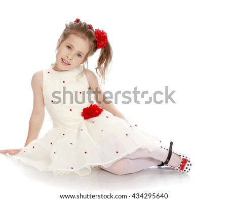 Adorable little girl dressed in white, long dress, sitting on the floor leaning on the arm - Isolated on white background