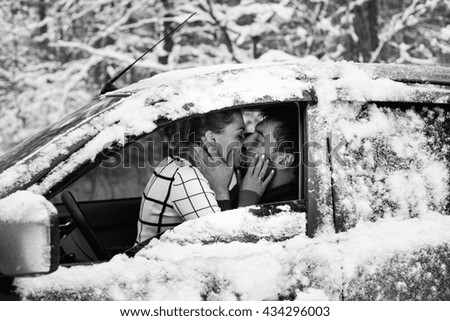 A couple sitting inside a snow car and kissing in a snow forest
