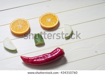 Face made of orange, apple, cucumber and pepper on a kitchen board, on yellow wooden background with copy space. Cheerful face, the concept of healthy eating.