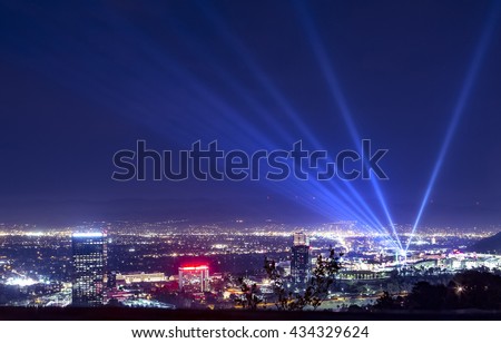 Huge bright powerful spotlight rays over the night sky panorama of Los Angeles city from Hollywood Hills.