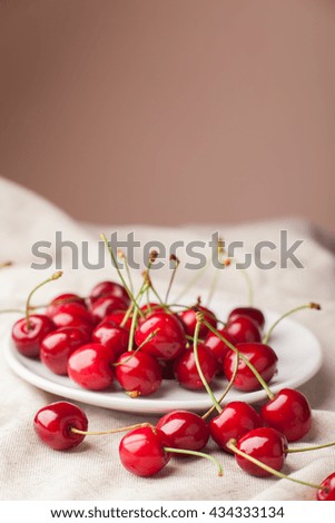 Fresh cherry lies in the white plate on the fabric