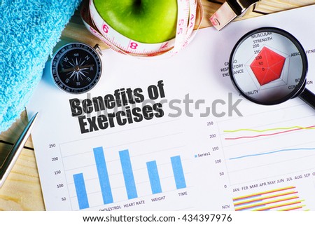 "Benefits of Exercise" black text on paper with magnifying glass on red spider bar on wooden table with compass, towel, green apple with measurement tape, and whistles - fitness, and healthy concept