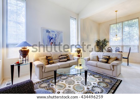 Bright white and blue living room with glass coffee table and rug. View of dining area.