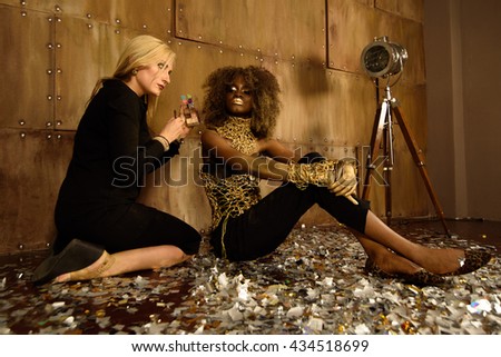 Artist applying makeup to beautiful african american model at photo shoot on floor in bright gold studio
