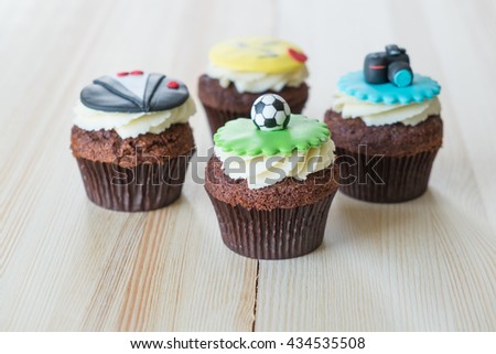 Delicious cupcakes with icons of ball, tuxedo, smiley and camera on it on wooden desk
