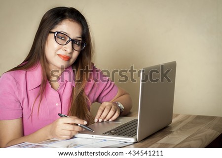 Indian young business woman working at the office. Businesswoman working at computer in office and looking at the camera. She is holding a black pen in her hand and wearing spectacles.  Royalty-Free Stock Photo #434541211