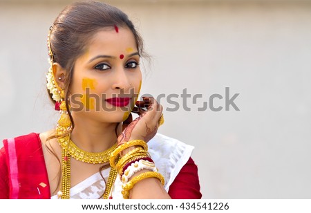Portrait of an Indian woman with gold jewelry and Turmeric. The woman looking at the camera and wearing red and white sari.  Royalty-Free Stock Photo #434541226