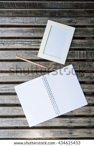 Vintage/Retro tone color of white picture frame, empty notebook and a pencil for write some memo put on the wooden background