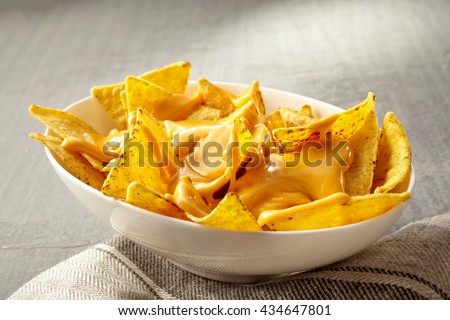 Single oval shaped white bowl of yellow tortilla chips topped with melted cheese placed on folded fabric napkin over tablecloth with copy space Royalty-Free Stock Photo #434647801