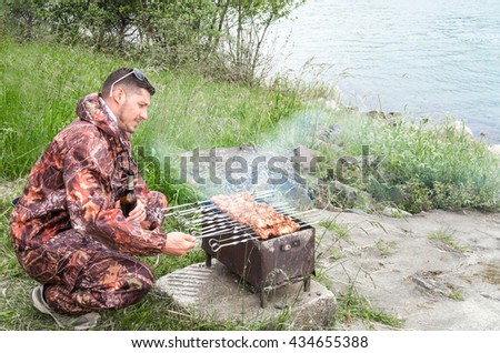 Male hunter preparing the meat near the lake. Hot food "Shashlik" in Russia.

