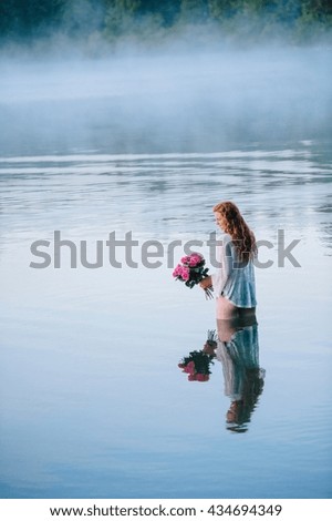 Young woman standing in misty lake holding bunch of pink roses