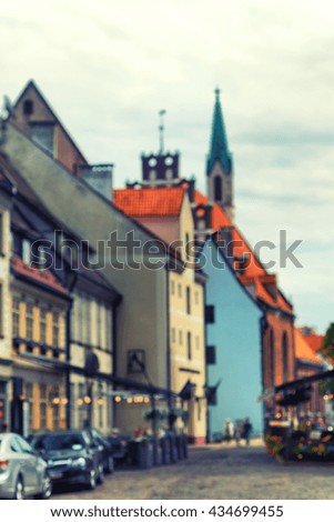 The street of cobblestones in the old town of Riga with cafes and building churches and houses with red tiled roof. Blurry