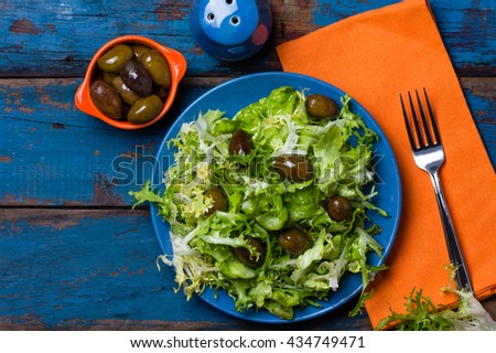 Vegetarian salad with lettuce and olives on blue plate. Colorful blue orange background. Top view. Healthy food