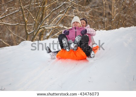 Mother and daughter having fun in winter by sliding down hill