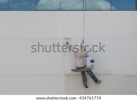 Painter hanging from harness painting a wall