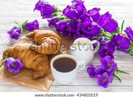 Cup of coffee, milk jar, croissants and bouquet of lilac bellflower flowers on rustic wooden background