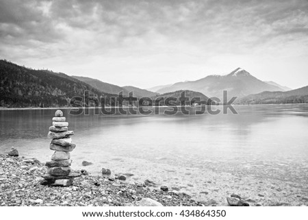 Balanced stone pyramide on shore of blue water of mountain lake. Children built pyramid from pebbles.  Poor lighting conditions.