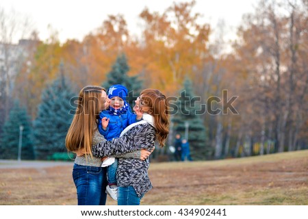 My mother and sister embrace and kiss the small son and brother. Cheerful family hugging in autumn. Cheerful boy in a blue cap and a jacket at the hands of her mother and sisters in a park in autumn.