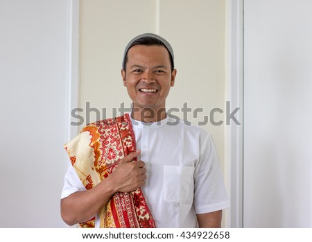 smiling asian muslim man bring prayer mat (sajadah) 