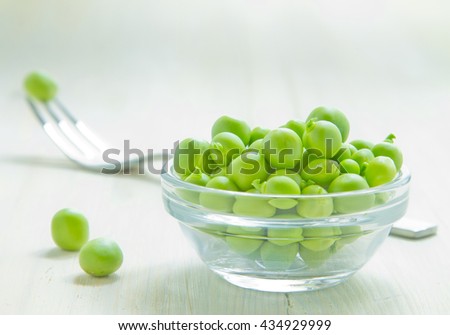 Green peas in glass plate on white wooden background