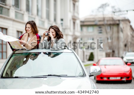 Two beautiful European women with map and camera leaned out of the car roof and enjoy the city in which they are traveling for the first time