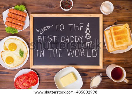 top down of concept Father's Day with handwritten text To The Best Daddy In World and pictured airplane, rocket on blackboard with setting breakfast over wooden background 