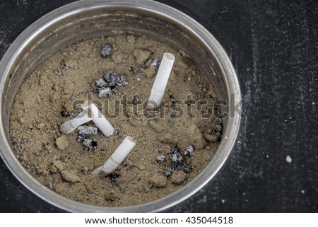 smoked cigarettes in a dirty sand ashtray filled with garbage lining on black  wooden Background, Pollution,Smoking, Danger.