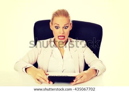 Shocked business woman sitting behind the desk with calculator 