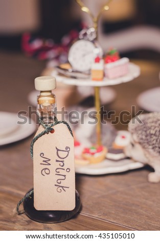 Magic Bottle with a tag that reads "drink me",  Tea Party on the Background. Dark fairytales concept. (vintage style)