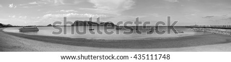 panorama view of sea and beach with traditional boat, bridge, long mountain in background, black and white picture style. Grain added