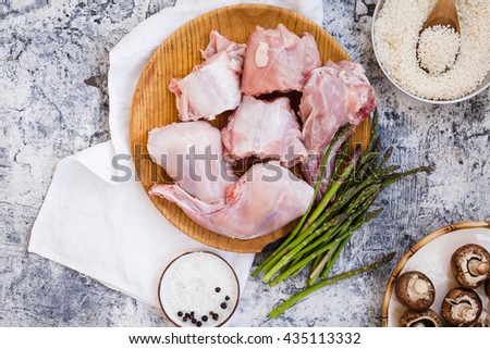 Raw rabbit sliced with asparagus on wooden board and spices y mushroom, rice over grey table.