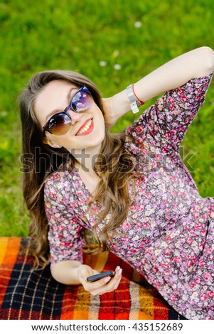 Ypung pretty woman in sunglasses with smartphone sitting on the grass in the park
