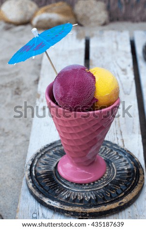 Mango and black-currant ice-cream in pink cone on the beach on old wooden background, summer vacation concept