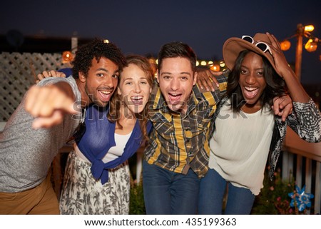 Multi-ethnic millenial group of friends taking a flash selfie photo with mobile phone on rooftop terrasse at night time