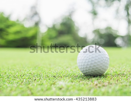 Golf ball on green with blurred pin flagstick and green tree background