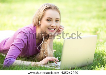 Nice looking young woman outdoors. Woman lying on grass, looking at camera and using laptop. Beautiful green park as a background