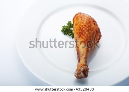 Closeup picture of roasted chicken leg on the white plate.