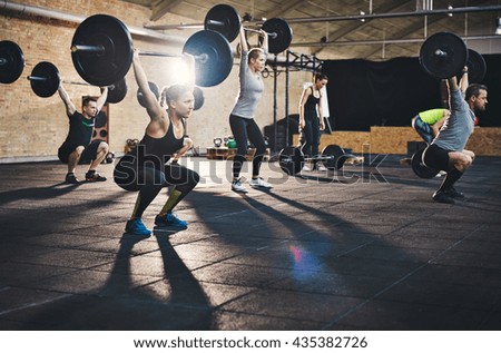 Fit young people lifting barbells over their heads looking focused, working out in a gym with other people Royalty-Free Stock Photo #435382726