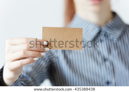 Selective focus. Cropped portrait of female entrepreneur or office worker in striped formal T-shirt and red hair holding a parchment business card with copy space for your text or advertising content
