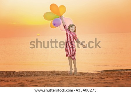 Happy girl with colorful balloons jumping on the sea at sunset. Toned colored image