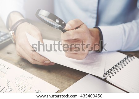 Businessman looking through a magnifying glass to documents Royalty-Free Stock Photo #435400450