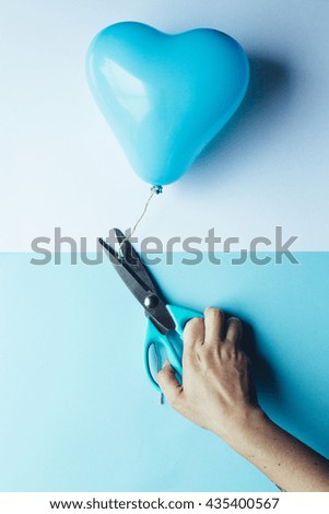 female hand using scissors to free a blue heart balloon, pastel background, trendy pop concept