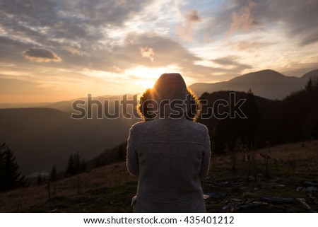 Lonely Girl watching sunset on the mountain. Girl with hood on her head looking at the sunset on top of the mountain. Cold weather. Autumn season. Autumn colors. Love concept.