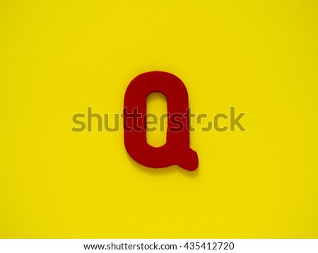 Capital red letter Q from wood on yellow background.