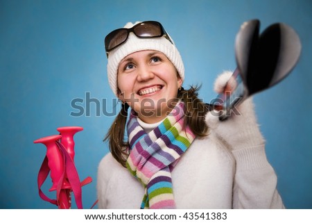 Portrait the beautiful woman in a cap with ski sticks in hands on a blue background