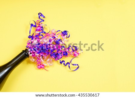 Party or celebration image of open champagne bottle with multi-colored curly ribbons spraying from top on yellow background. Copy space right side.