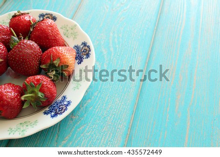 Strawberries in white plate on wooden blue desk. Stock photo.