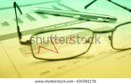 Glasses and pen on financial chart and graph, success concept, green and yellow tone