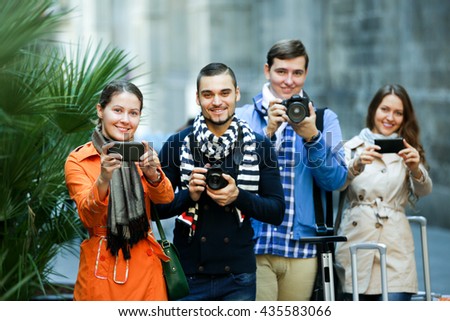 Group of beautiful young friends walking through street with camera and smartphone. Focus on the left woman