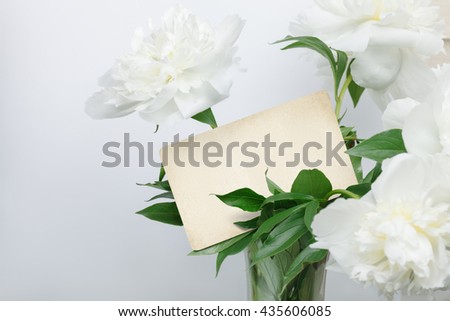White peonies bouquet with retro blank card inside. Ready for your text.